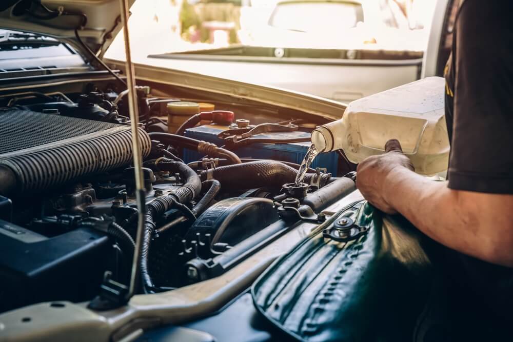 Mechanic pouring antifreeze coolant into a car engine radiator